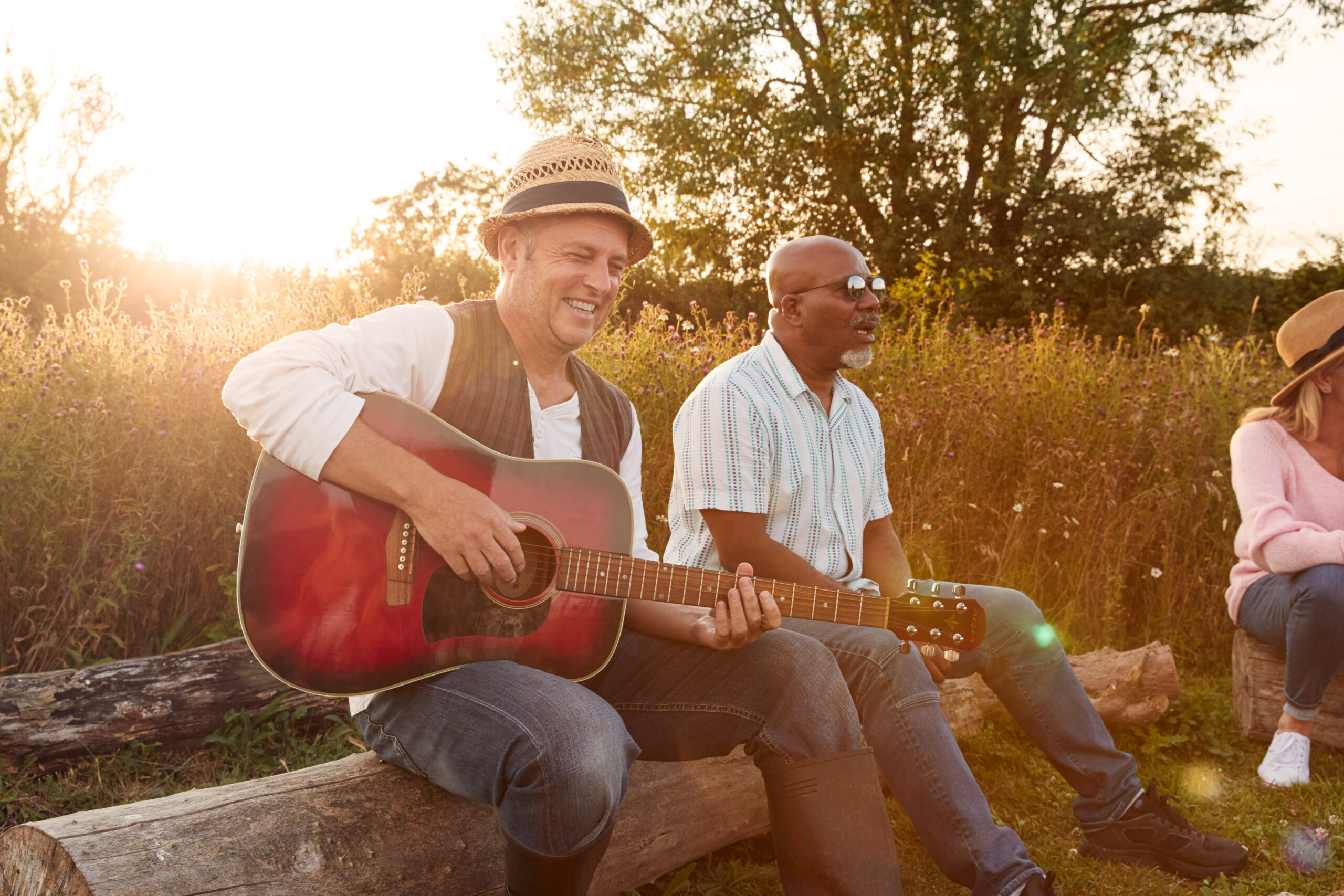 Group Of Mature Friends Sitting Around Fire And Singing Songs At Outdoor Campsite